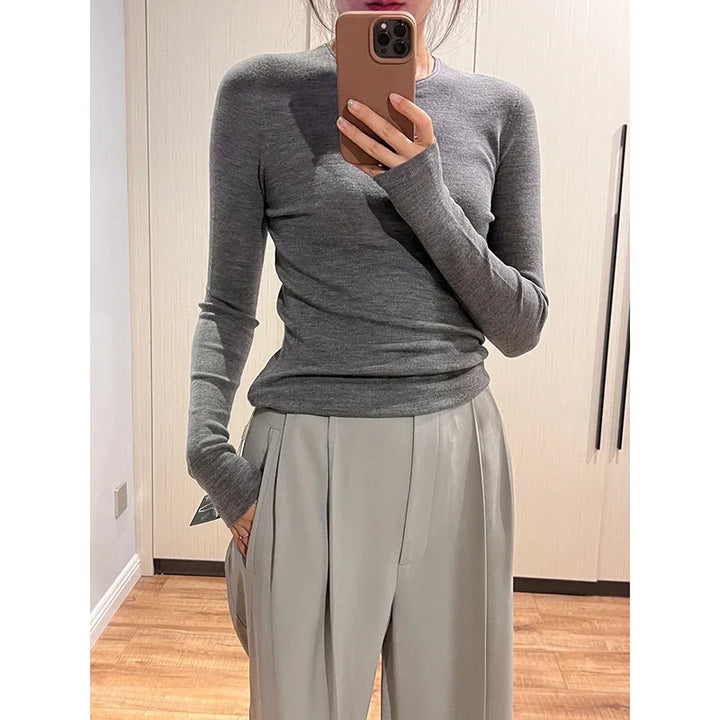Person wearing fitted grey long-sleeve sweater and light beige pleated trousers taking mirror selfie