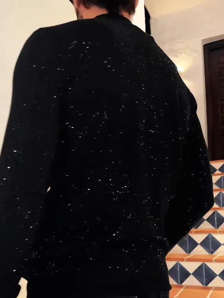 Man wearing black glittery sweater standing indoors near staircase with blue and white tiles