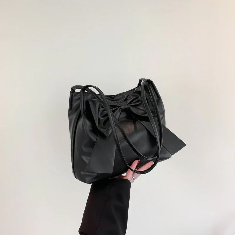 Black leather handbag featuring a large decorative bow held against a plain light background