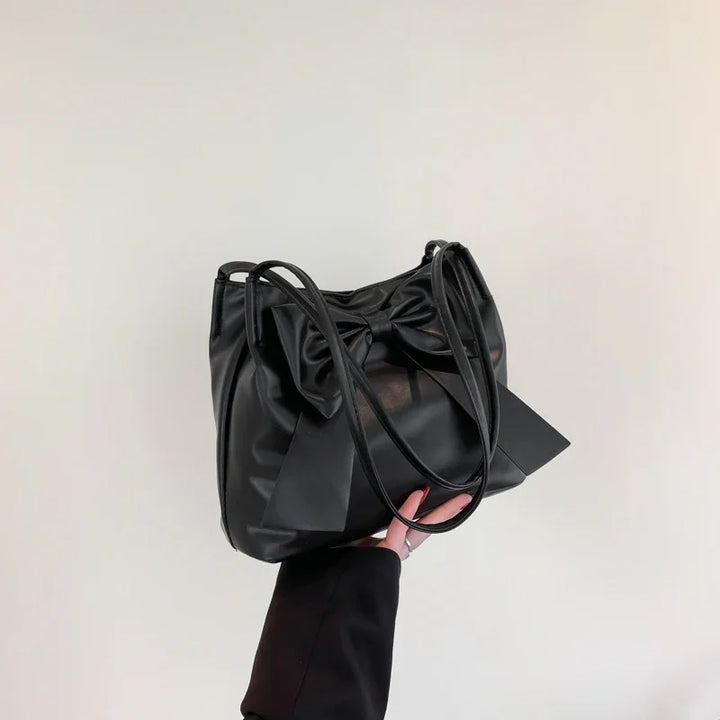 Black leather handbag featuring a large decorative bow held against a plain light background
