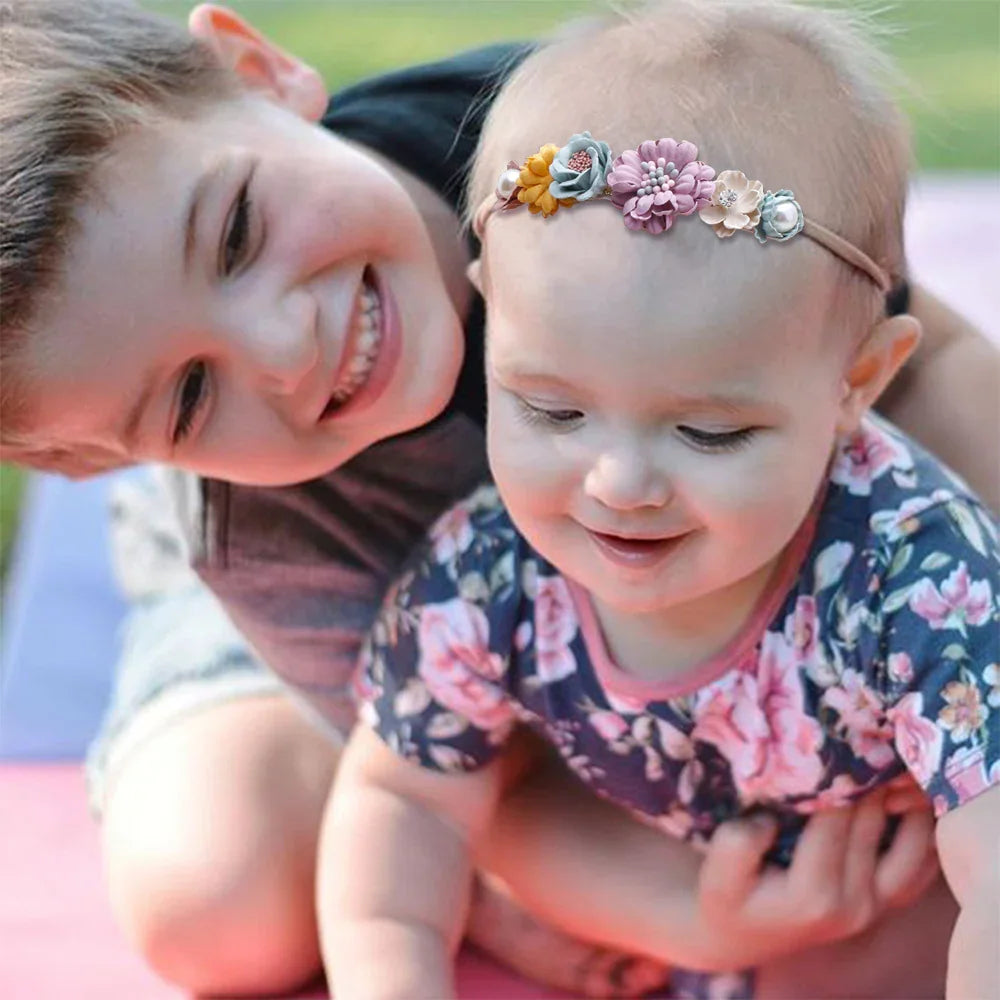 Smiling boy hugging baby girl wearing floral headband and dress outdoors on blanket