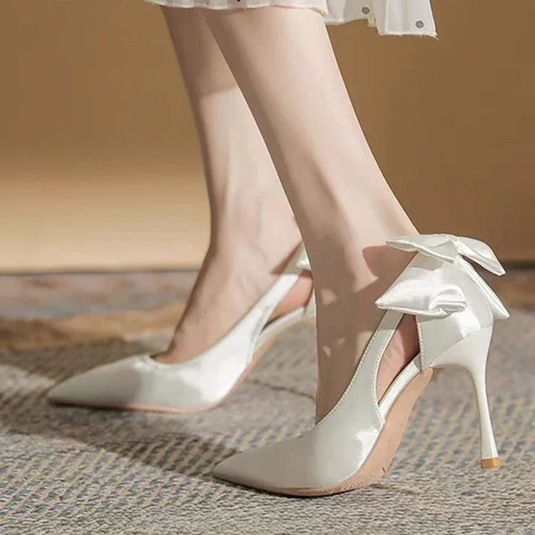 Elegant white high heel slingback shoes with satin bow detail on carpeted floor