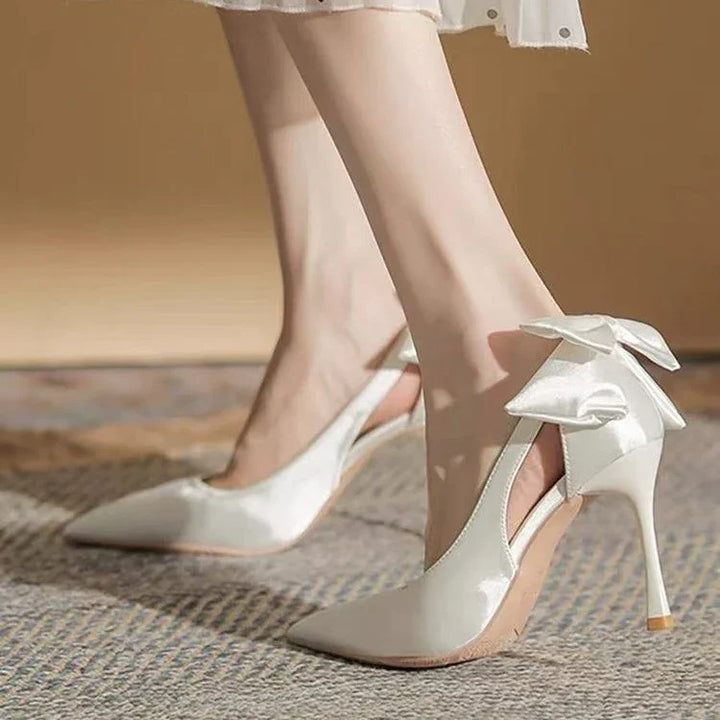 Elegant white high heel slingback shoes with satin bow detail on carpeted floor