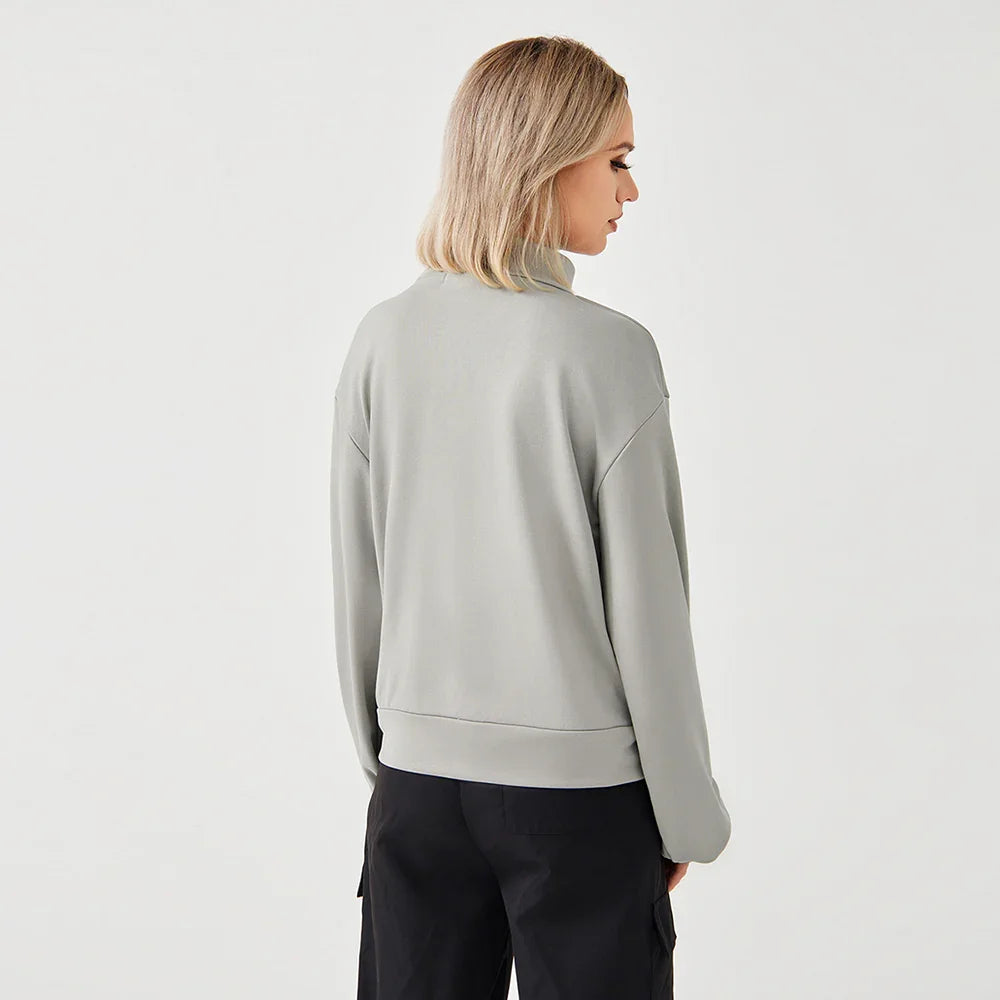 Woman wearing light gray sweatshirt and black pants, viewed from back on plain white background