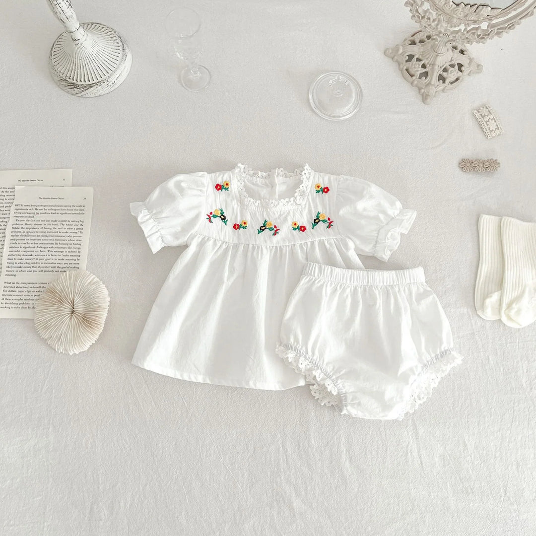 White baby dress and matching bloomers with embroidered flowers and lace trim on white background