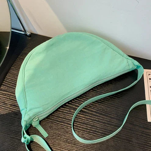 Mint green half-moon shaped crossbody bag on dark wooden surface next to mirror and paper