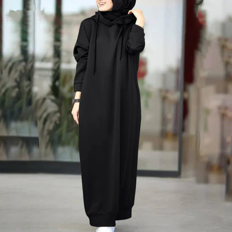 Woman wearing a black modest abaya dress and hijab, standing outdoors with blurred background
