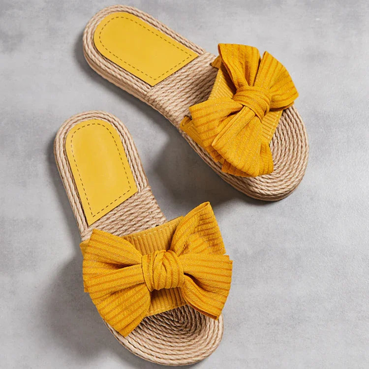 Yellow bow espadrille slides with braided jute soles on gray background