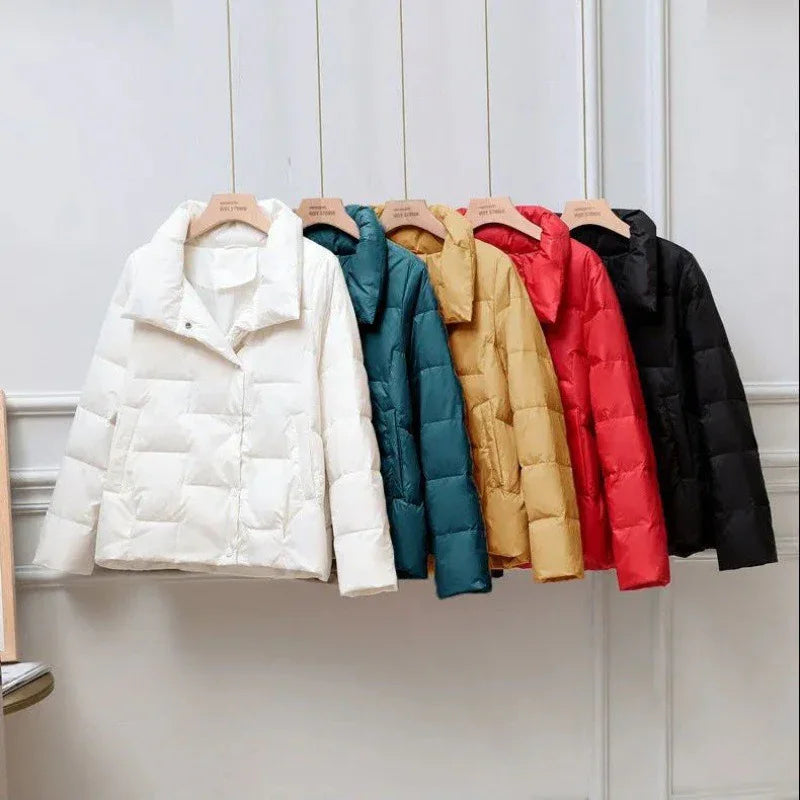 Row of five padded winter jackets in white, teal, mustard, red, and black hanging on wooden hangers indoors