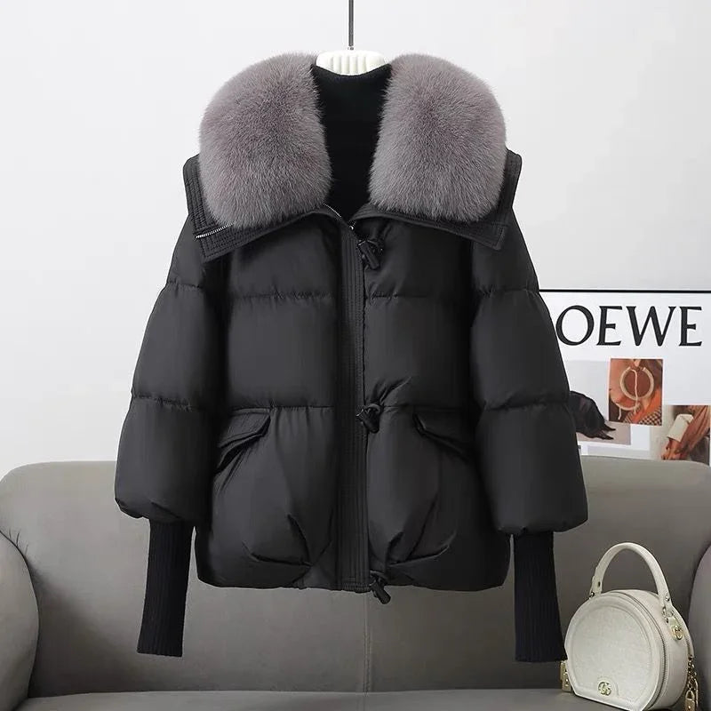 Black puffer jacket with large gray faux fur collar displayed on hanger over gray sofa