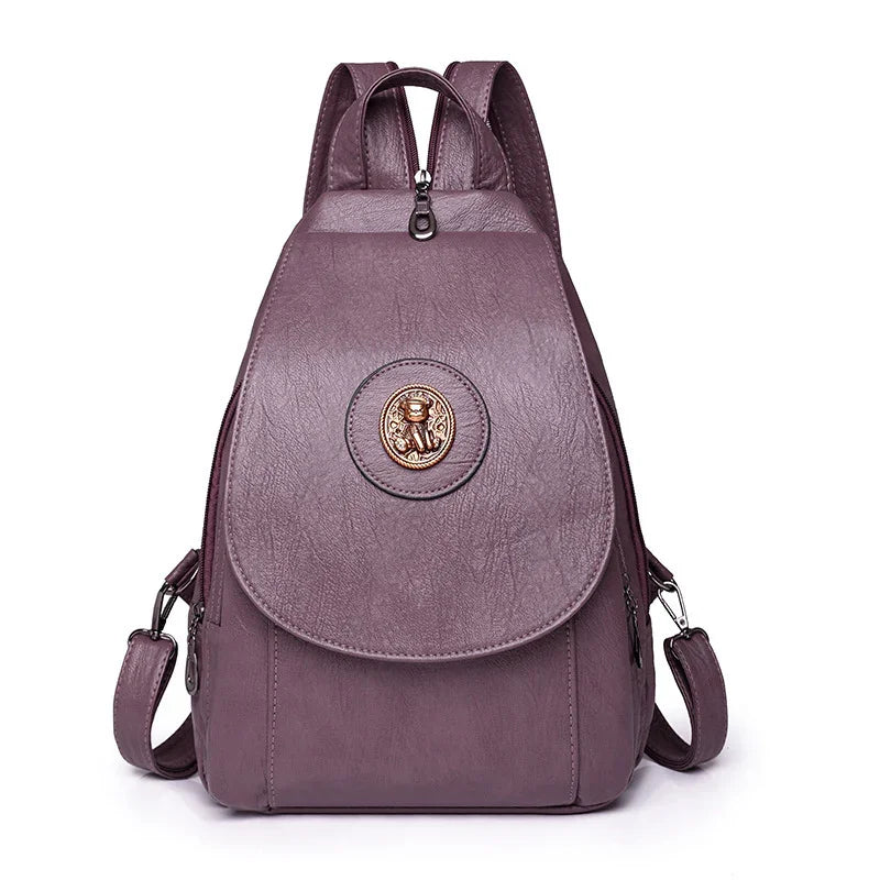 Purple leather backpack with a front flap and round emblem featuring a teddy bear design