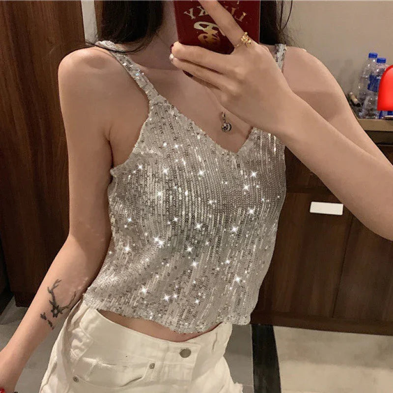 woman wearing sparkling silver sequin tank top and white pants taking selfie in indoor setting