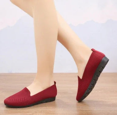 Close-up of legs wearing red slip-on casual shoes with textured fabric and black soles on wooden floor