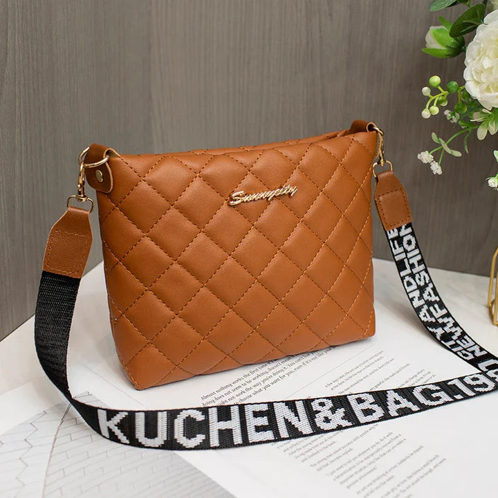 Brown quilted leather handbag with black and white KUCHEN&BAG adjustable strap on a white surface