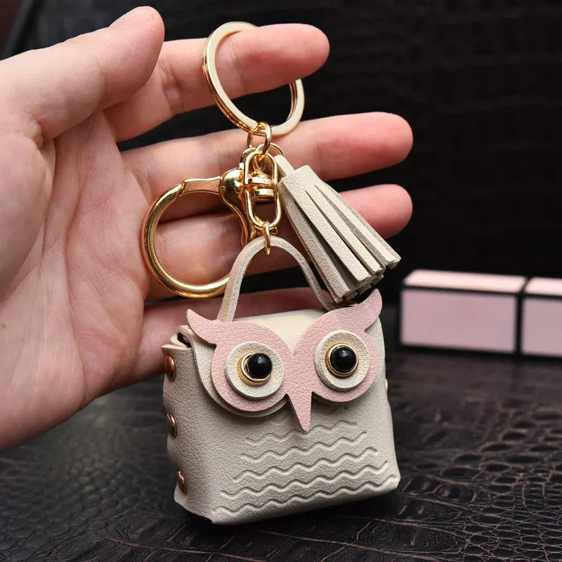 Hand holding beige owl-shaped leather keychain with gold hardware and tassel accessory