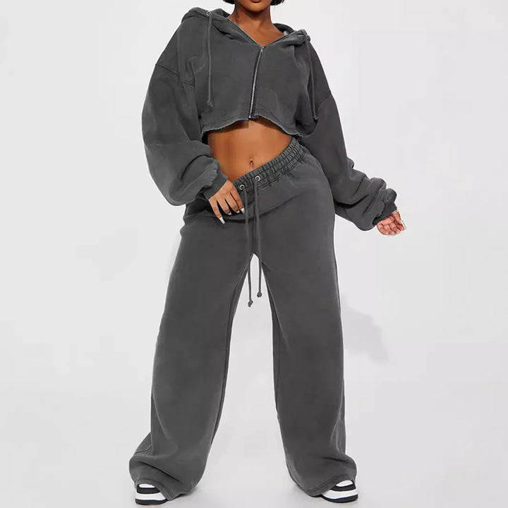 Woman wearing dark gray cropped hoodie and wide-leg sweatpants with sneakers on white background