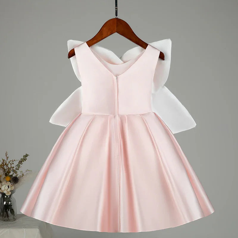 Light pink satin flower girl dress with large white bow on back, displayed on wooden hanger