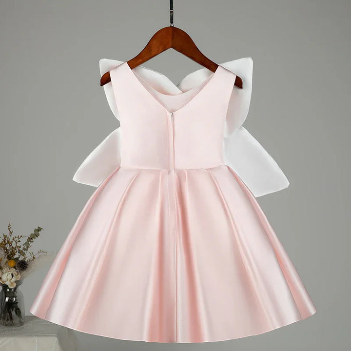 Light pink satin flower girl dress with large white bow on back, displayed on wooden hanger