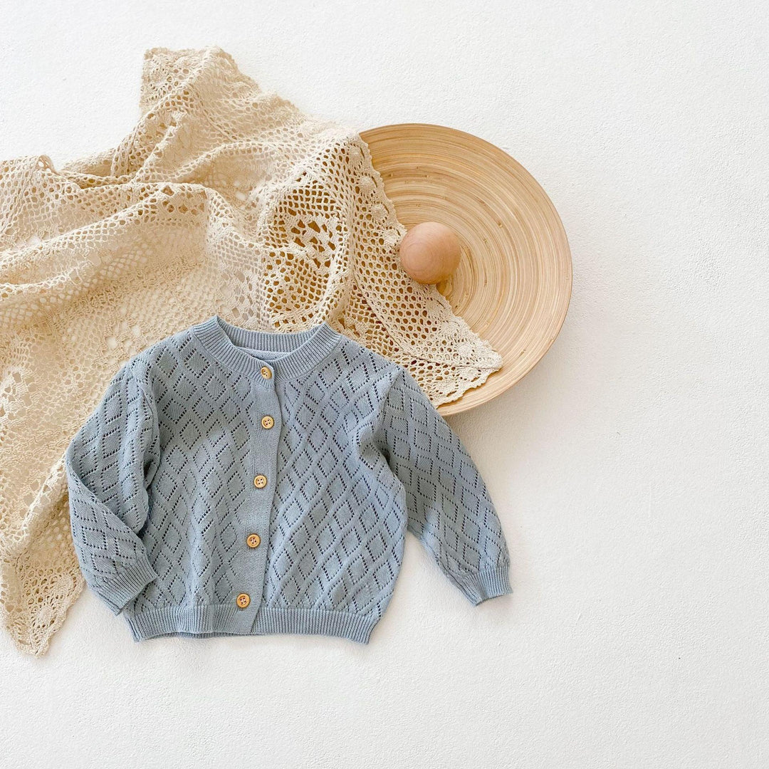 Light blue knitted baby cardigan with wooden buttons on beige lace cloth and wooden plate