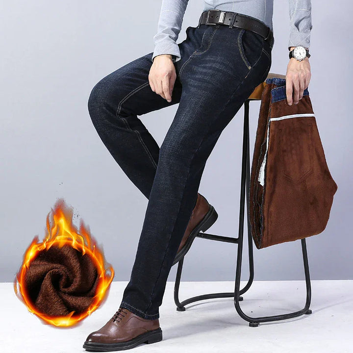 Man wearing dark blue jeans and brown shoes sitting on stool holding warm lined brown pants with fleece fabric and flame graphic