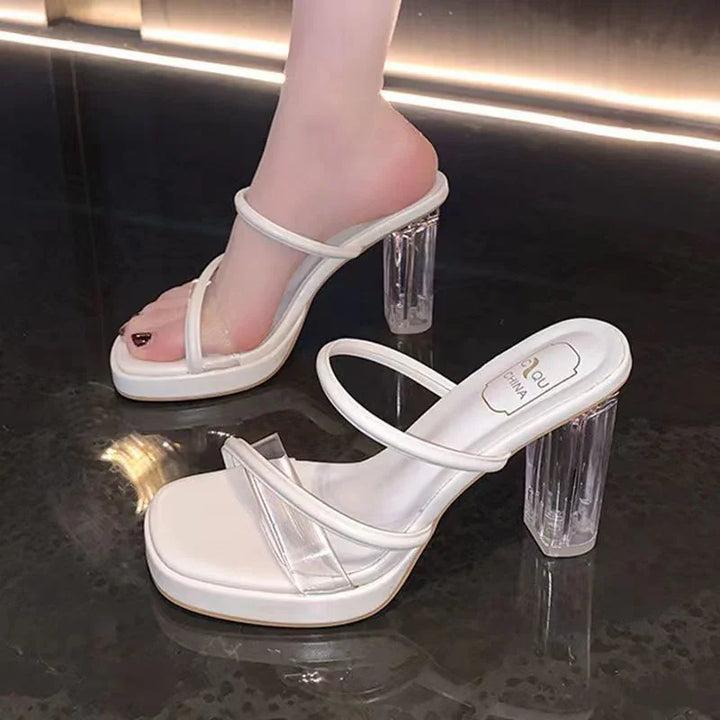 White strappy high-heeled sandals with clear block heels on shiny dark floor