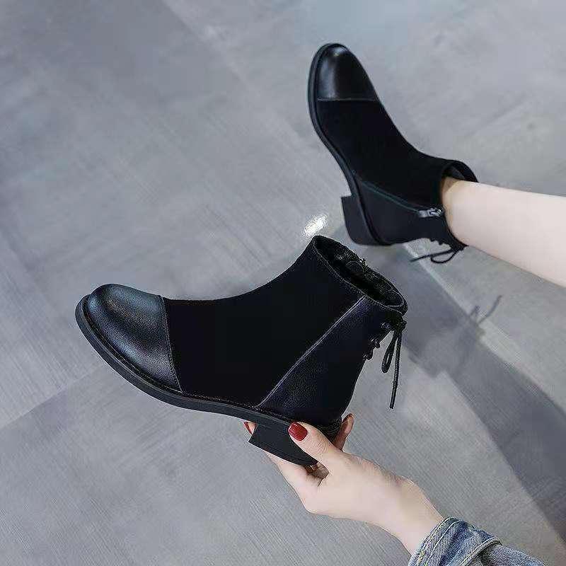 Black leather ankle boots with block heels worn and held by a person on gray floor