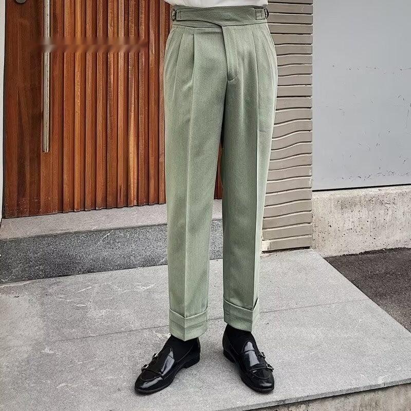 Men's sage green pleated trousers paired with black leather loafers in outdoor urban setting