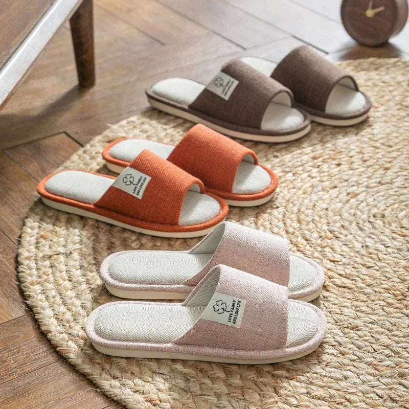 Three pairs of cozy indoor slippers in beige, orange, and brown on a woven round rug with wooden floor