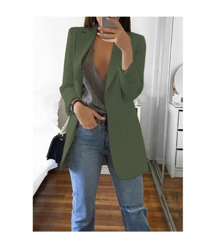 Woman taking mirror selfie wearing olive green blazer, gray v-neck top, and ripped blue jeans in bedroom