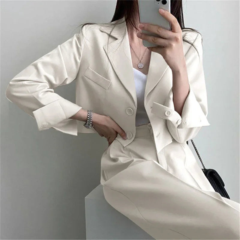 Woman wearing a cream-colored cropped blazer and matching skirt, taking a mirror selfie