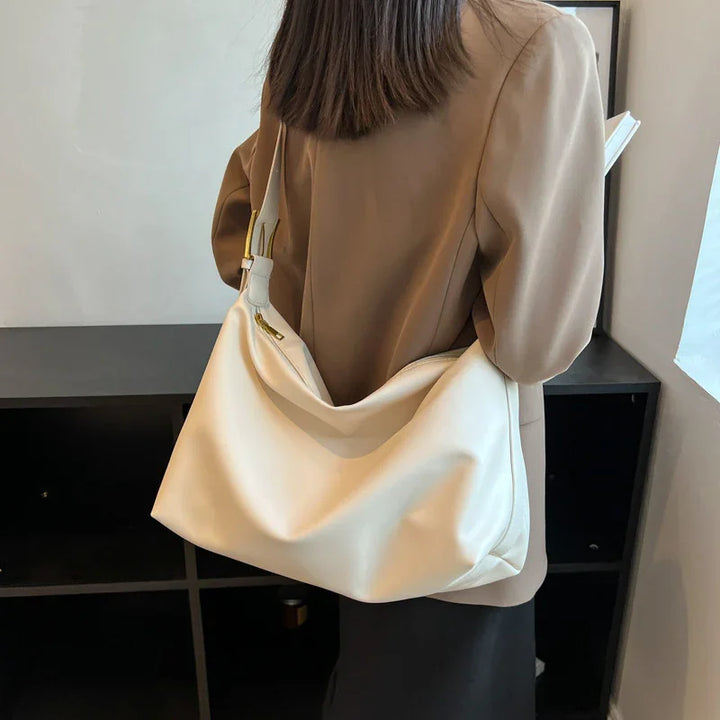 Woman wearing beige blazer holding large white leather shoulder bag indoors