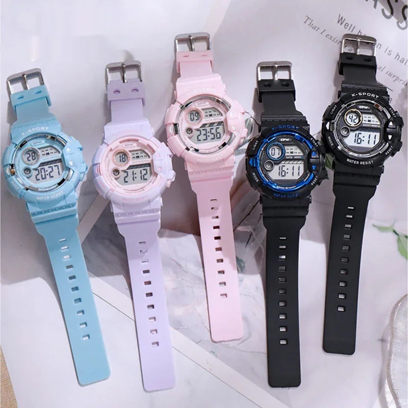 Five digital K-Sport watches in blue, purple, pink, black with blue, and all black displayed on a marble surface