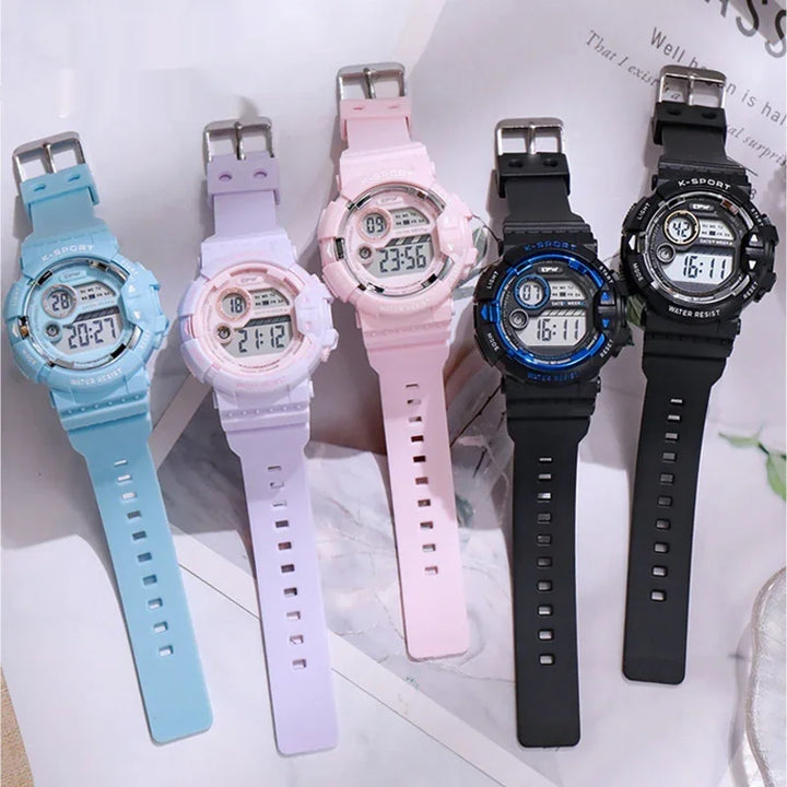 Five digital K-Sport watches in blue, purple, pink, black with blue, and all black displayed on a marble surface