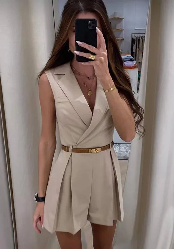 Woman taking mirror selfie wearing beige sleeveless blazer dress with pleated shorts and brown belt