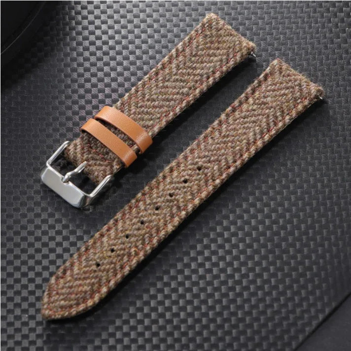 Brown tweed fabric watch strap with leather loops and silver buckle on black textured surface