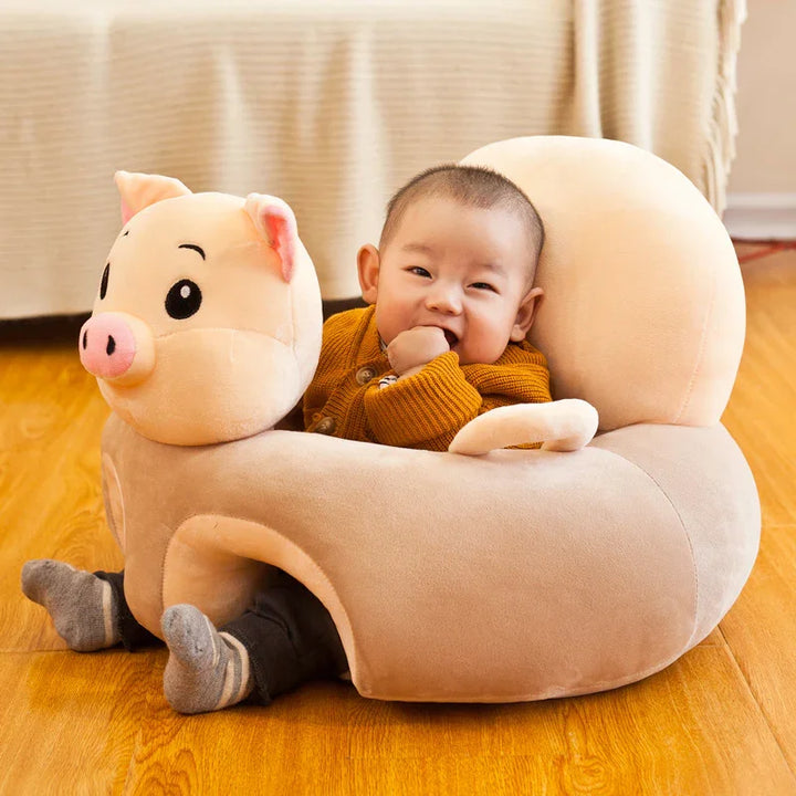 Smiling baby sitting in a beige pig-shaped plush seat on wooden floor, wearing brown sweater
