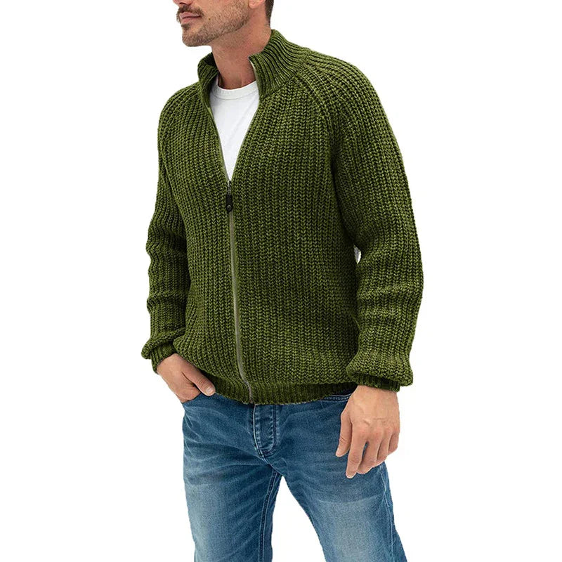 Man wearing olive green chunky knit zip-up sweater with blue jeans on white background