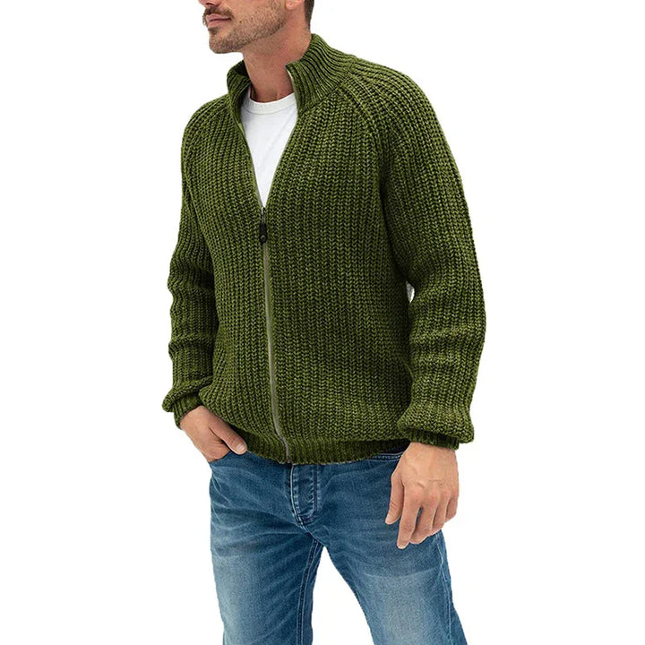 Man wearing olive green chunky knit zip-up sweater with blue jeans on white background