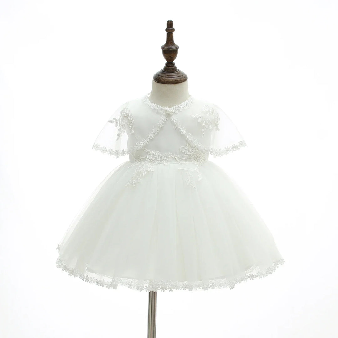 Elegant white baby girl dress with lace details on sleeves and hem, displayed on wooden mannequin