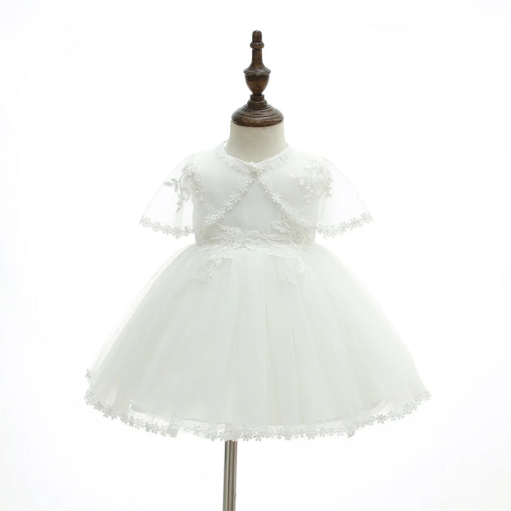 Elegant white baby girl dress with lace details on sleeves and hem, displayed on wooden mannequin