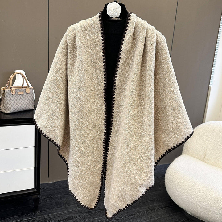 Beige textured shawl with black trim displayed on a black mannequin in a modern room