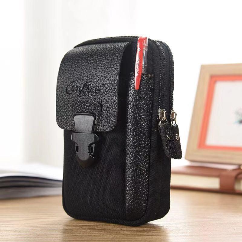 Compact black fabric and leather pouch with dual zippered compartments and front buckle pocket holding a red pen