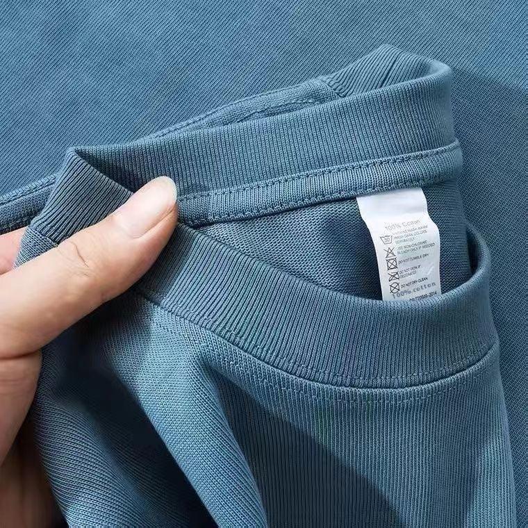 Close-up of hand holding blue cotton t-shirt collar showing care label with washing instructions
