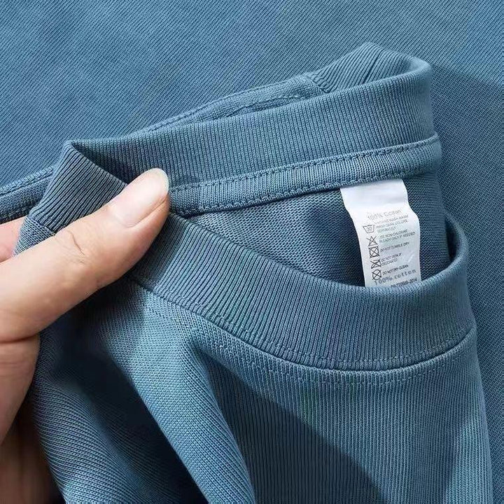 Close-up of hand holding blue cotton t-shirt collar showing care label with washing instructions