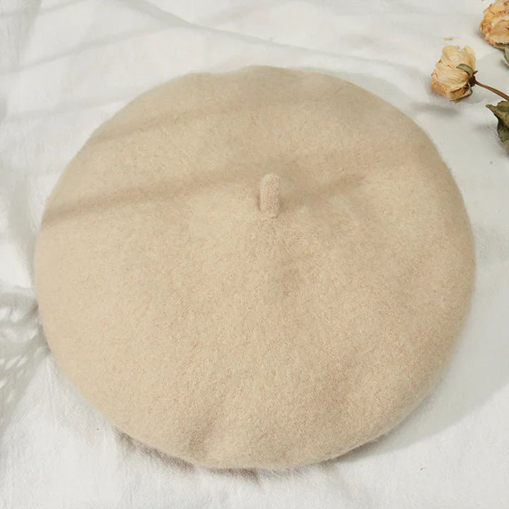 Beige wool beret hat on white fabric with dried flowers nearby