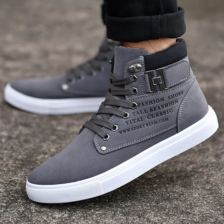 gray high-top fashion sneakers with white sole and black collar worn with black pants on pavement