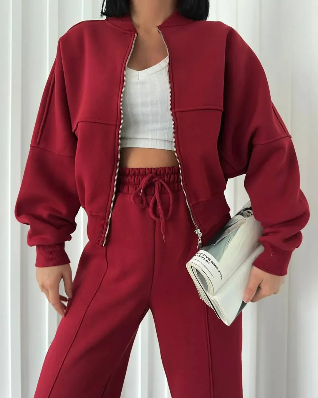 Woman in red zip-up jacket and matching red drawstring pants holding a rolled magazine