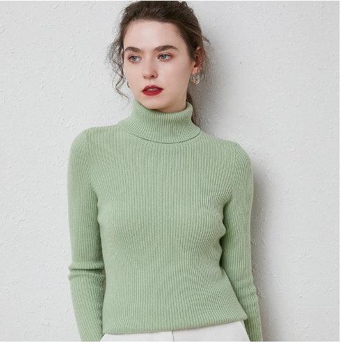 Woman wearing light green ribbed turtleneck sweater against white textured wall