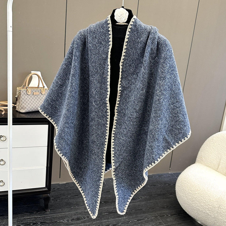 Blue knitted shawl with white trim displayed on a black mannequin in a modern room