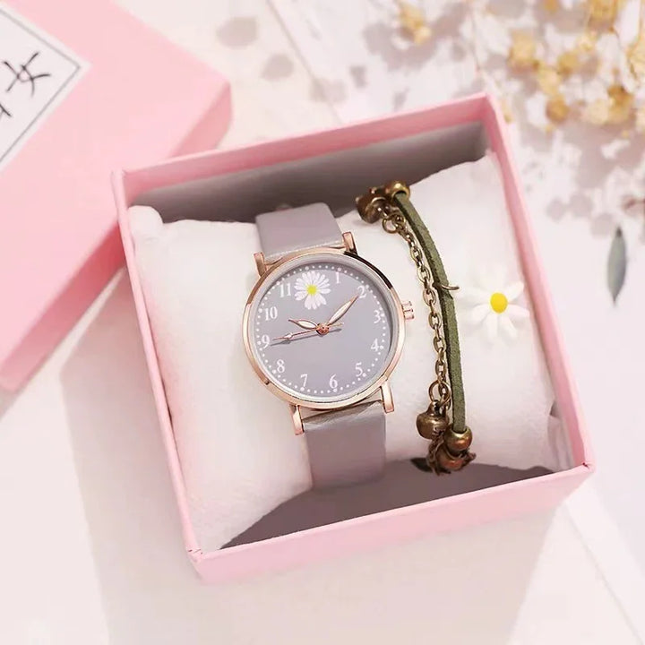 Wristwatch with grey strap and daisy design in pink gift box alongside green bracelet with charms